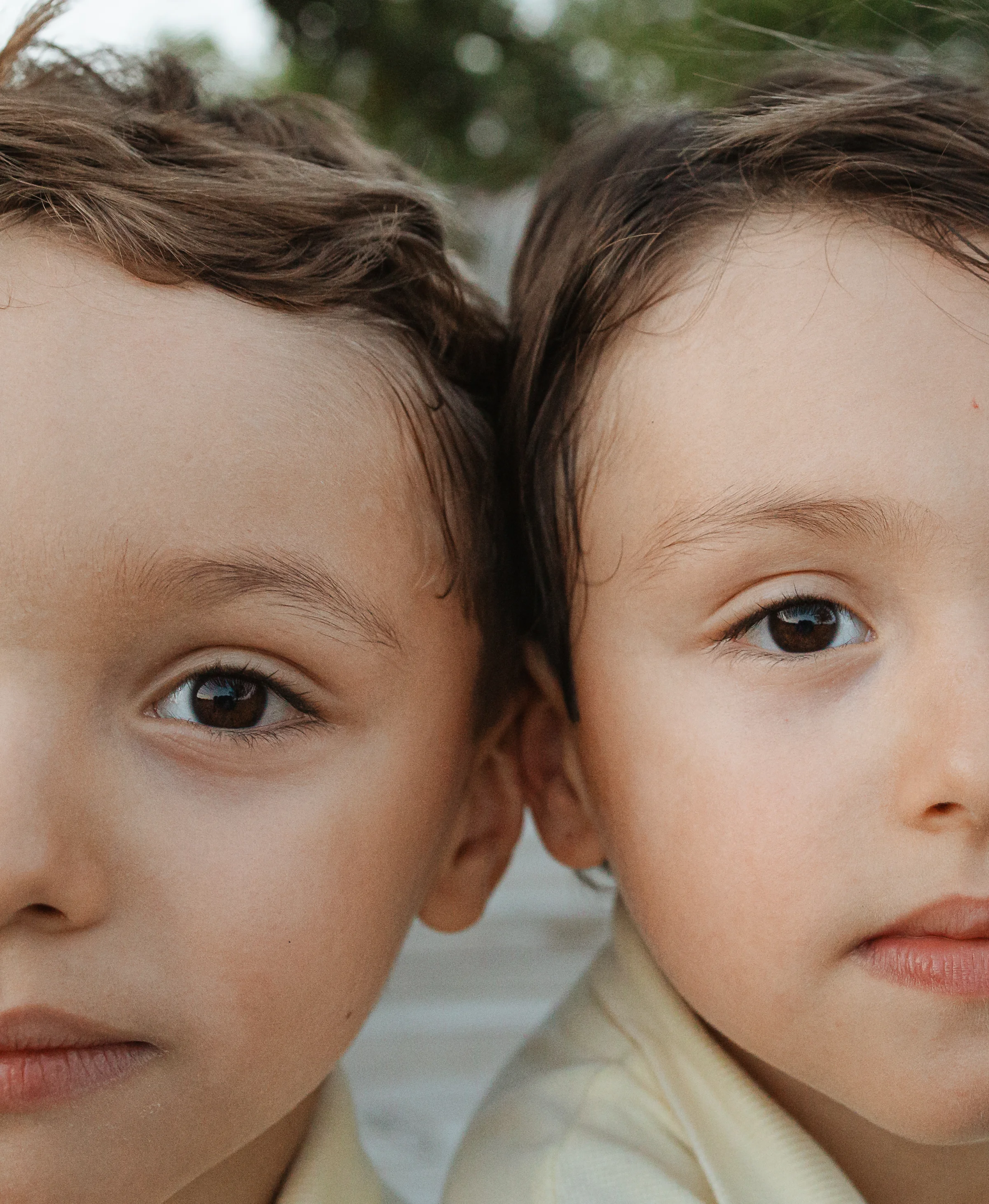 Close up of two brown eyed children with wavy hair resting head to head in soft natural light.
