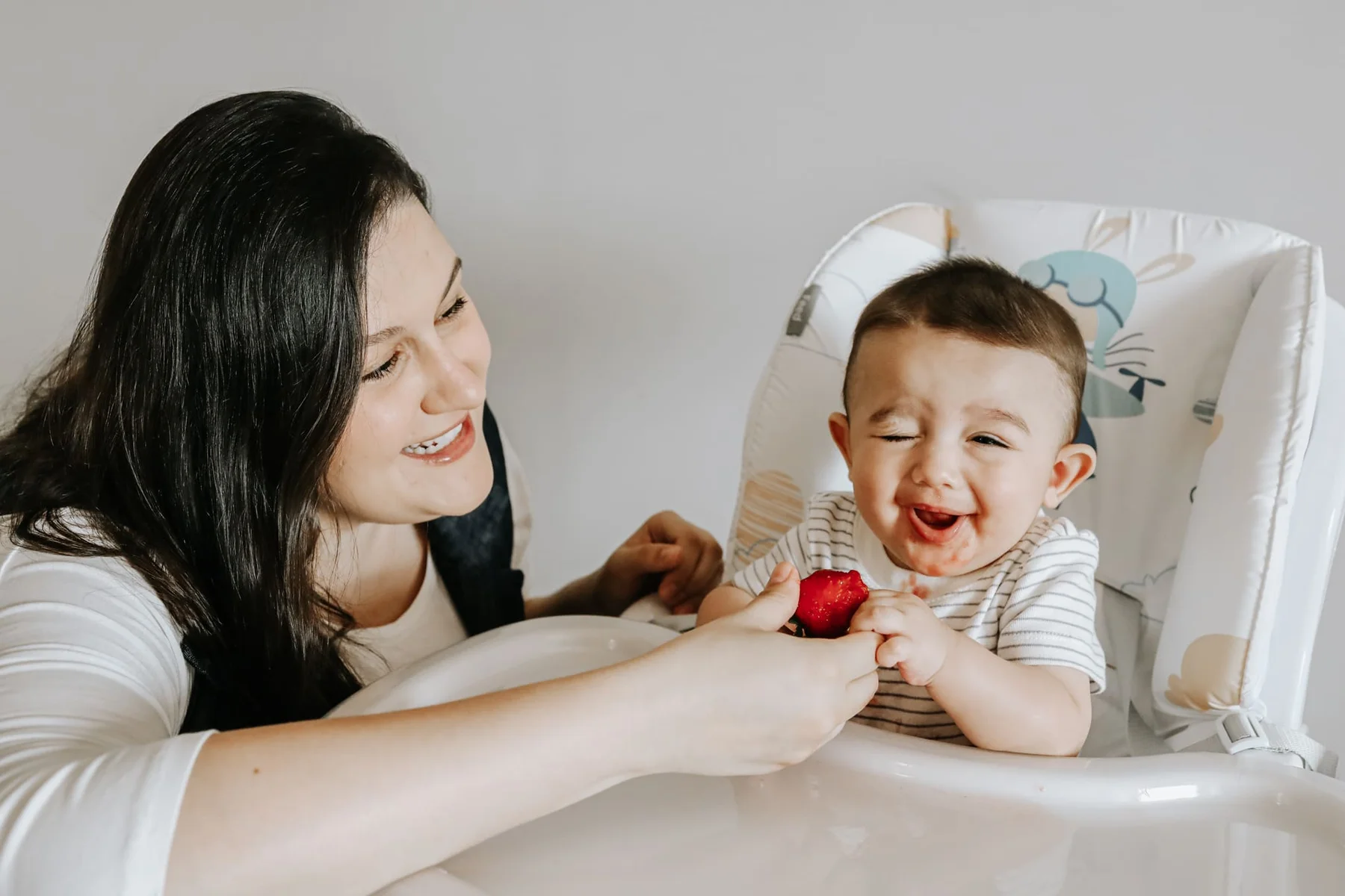 Mother laughing with her baby during mealtime in the high chair