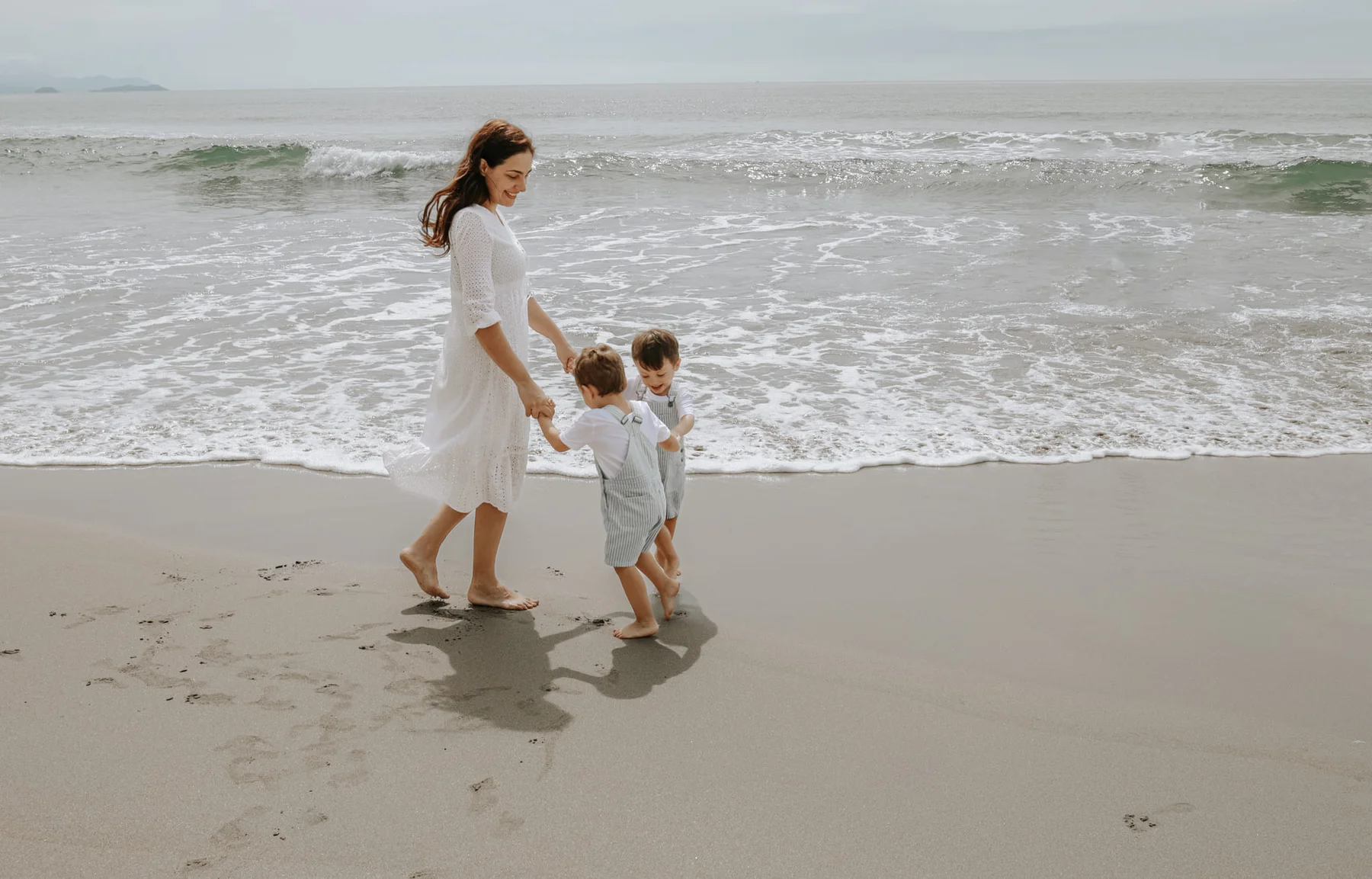 Mother walking hand in hand with her two sons along the beach