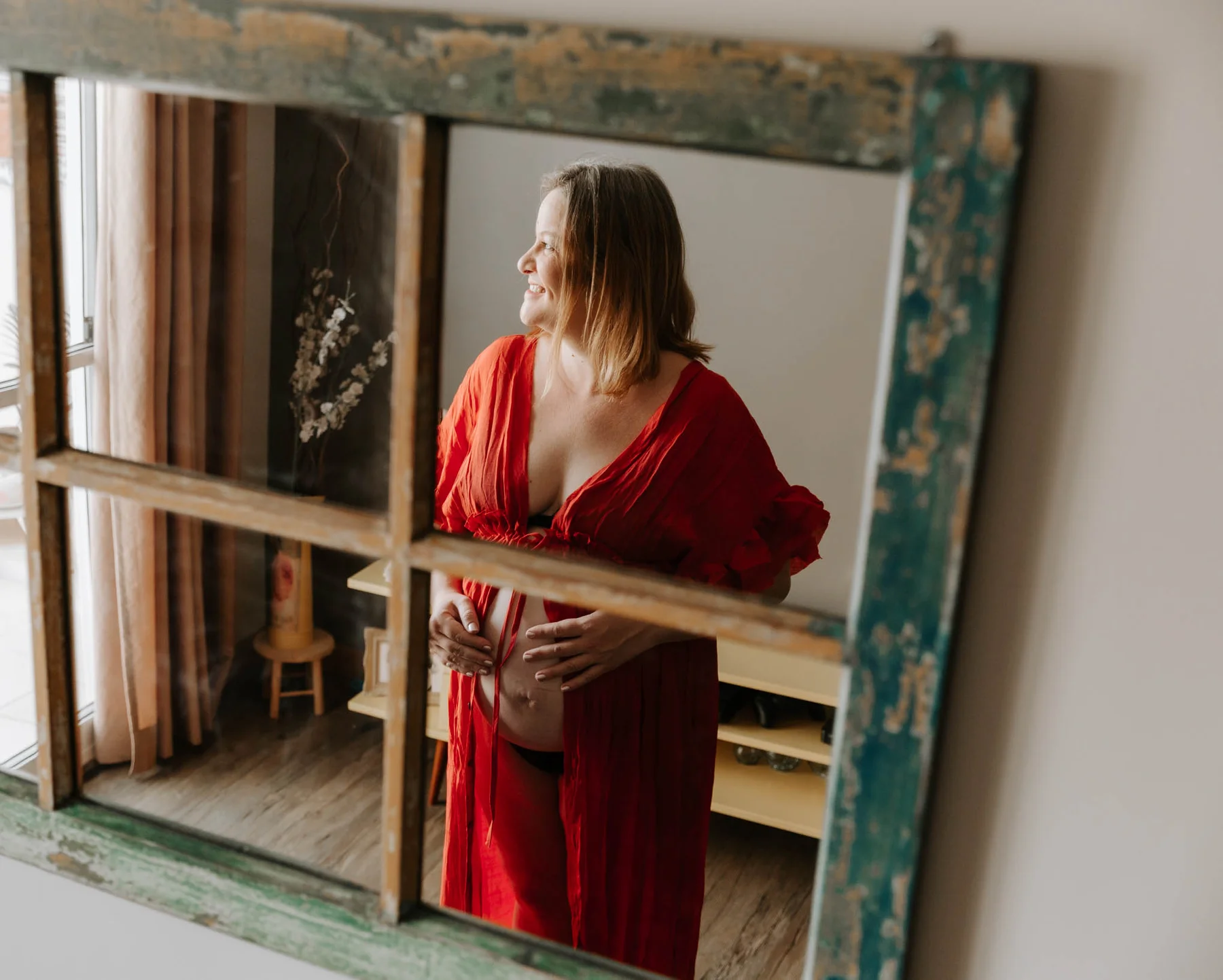 Expecting mother in a flowing red dress, reflected in an antique mirror